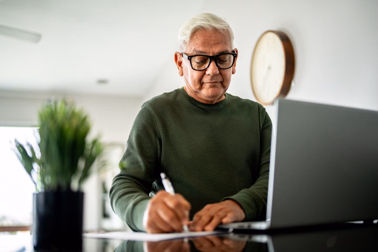 An elderly man writing in front of his computer